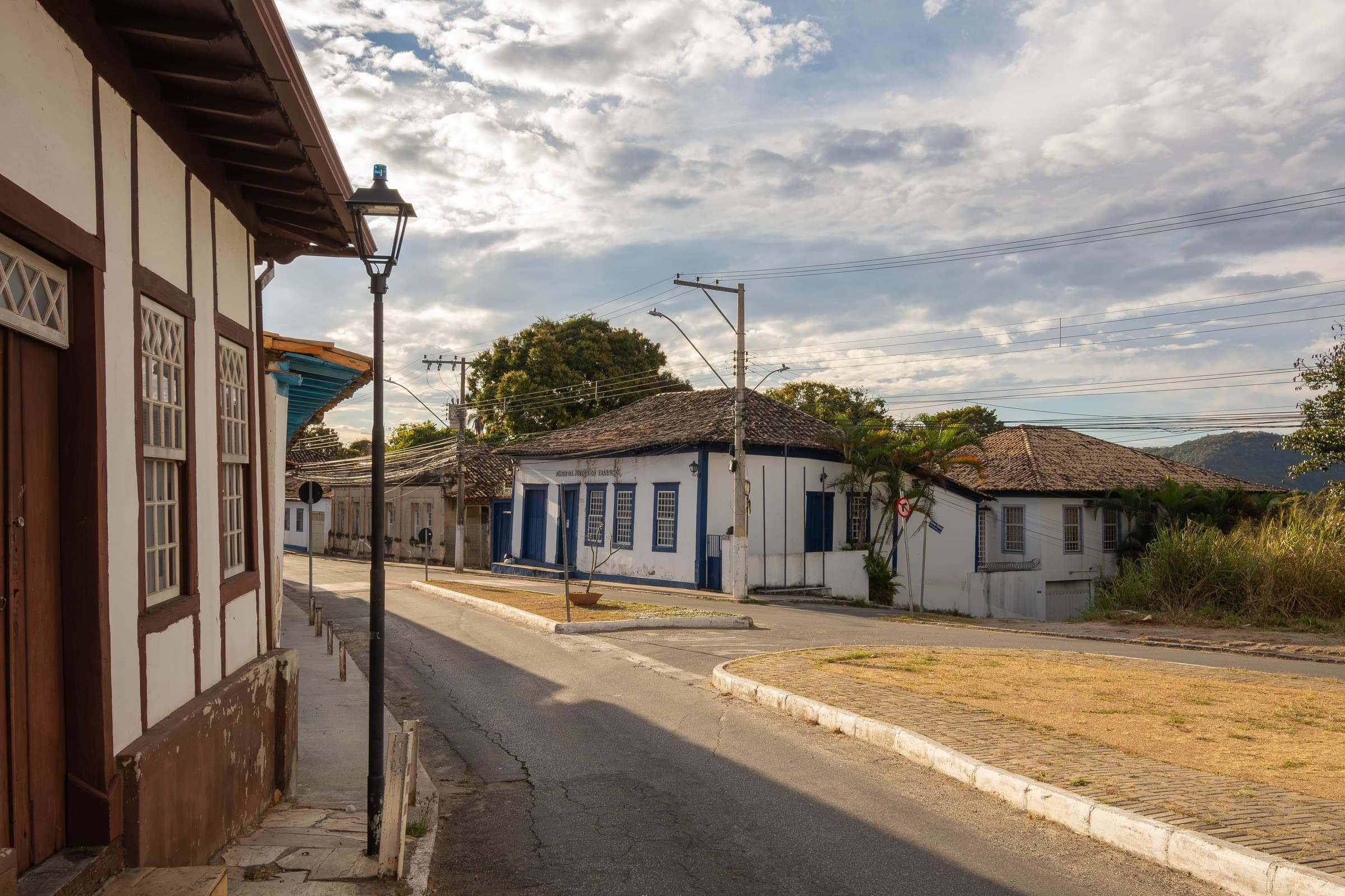 Rua de cidade pequena do interior de Minas, com casario colonial, poste de luz e morros ao fundo